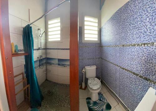 a bathroom with a toilet and a blue tiled wall at Bungalows Mathilde-non fumeur in Bouillante