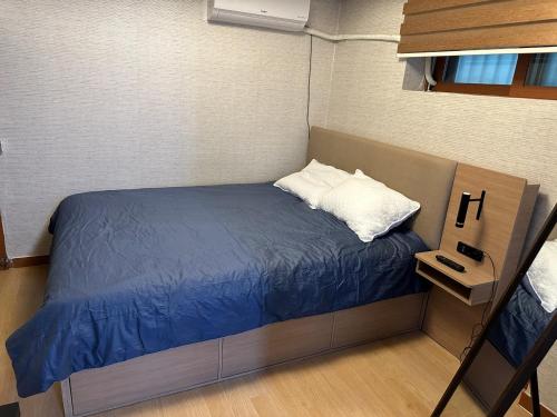 a small bed with a blue blanket and white pillows at Hwarangdae Station One-room House in Seoul