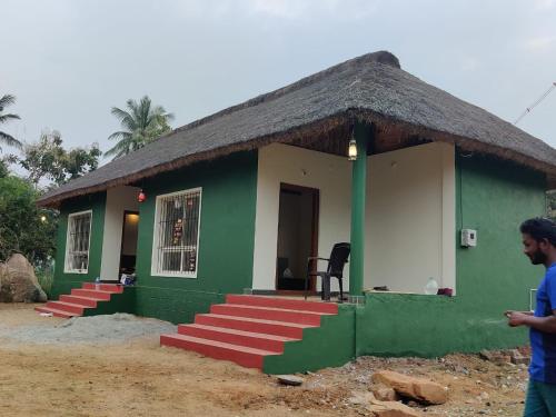 a small green and white house with a thatch roof at ATHARV GUEST HOUSE in Hampi