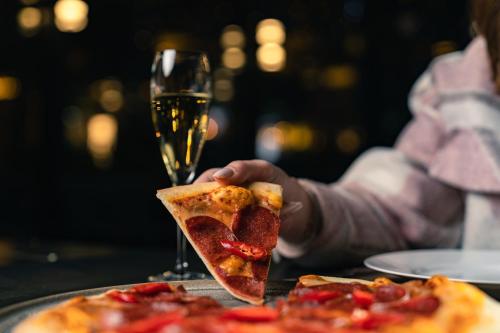 a person holding a slice of pizza and a glass of wine at The Abdali Boulevard Hotel in Amman