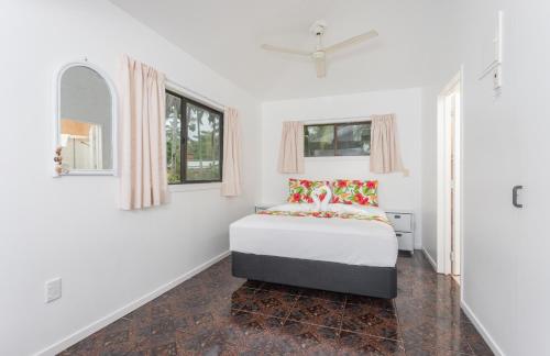 a white bedroom with a bed and two windows at Bella Beach Bungalows in Rarotonga