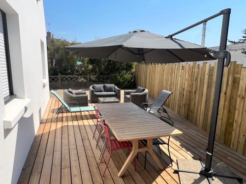 une terrasse en bois avec une table et un parasol dans l'établissement La Maison Des Sables Blancs, à Loctudy