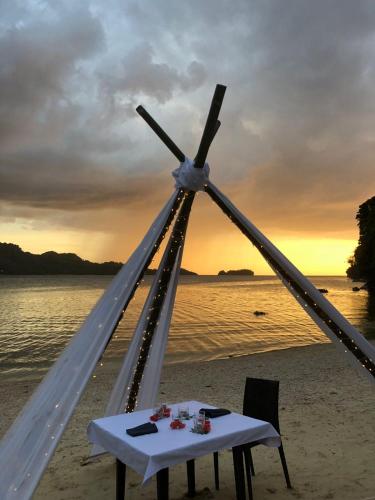 a dinner table on the beach with the sunset in the background at Bugana Beach and Dive Resort in Manlocahoc