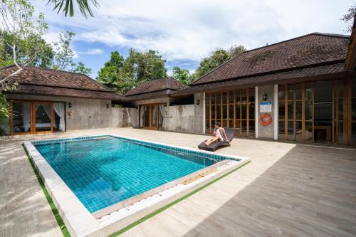 a man sitting next to a swimming pool next to a house at Bor Saen Pool Villa in Bor Saen
