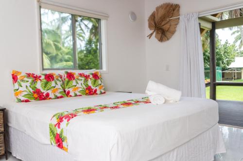 a white bedroom with a large bed with floral pillows at Bella Beach Lodge in Rarotonga
