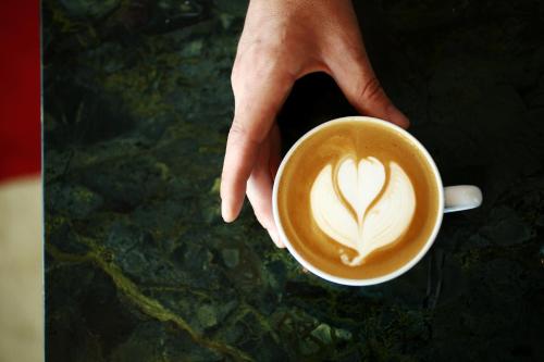 a person holding a cup of coffee with a heart painted on it at The Durham Hotel in Durham