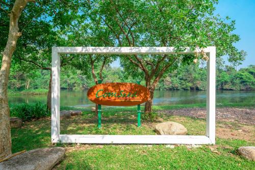 a bench sitting in the grass next to a river at Comsaed River Kwai Resort in Kanchanaburi