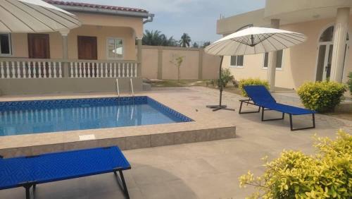 a swimming pool with two blue chairs and an umbrella at pavillon « lilas » à dagué-togo in Dagé