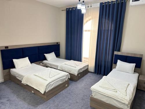 two beds in a room with blue curtains at Silver Hotel in Samarkand