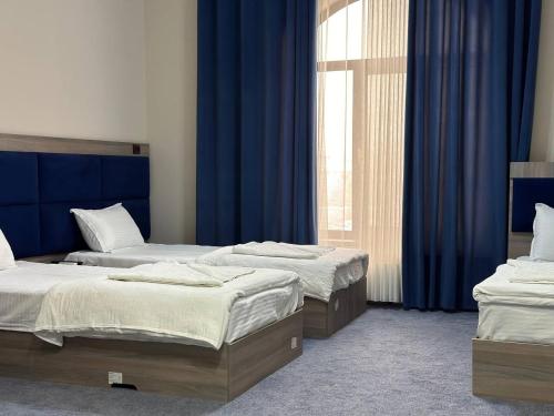 two beds in a room with blue curtains at Silver Hotel in Samarkand
