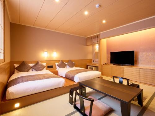 two beds in a room with a table and a tv at Temple Town Hotel WAQOO Horyuji in Ikaruga