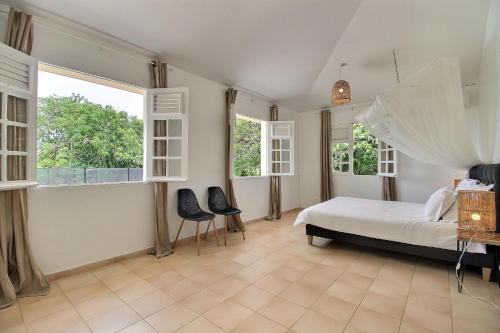 een slaapkamer met een bed met 2 stoelen en 2 ramen bij Villa Flamboyant in Le François