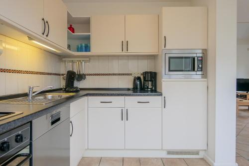 eine Küche mit weißen Schränken und einer Mikrowelle in der Unterkunft Vakantiehuis Duyngroet - Landal park Ooghduyne Julianadorp aan Zee in Julianadorp