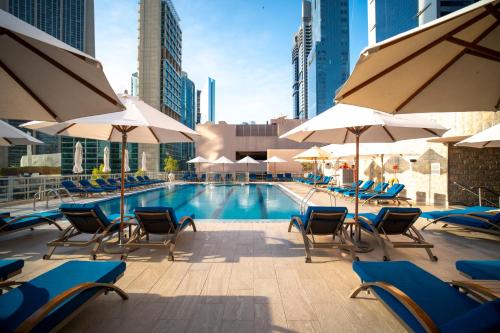 a swimming pool with chairs and umbrellas at Rose Rayhaan by Rotana - Dubai in Dubai