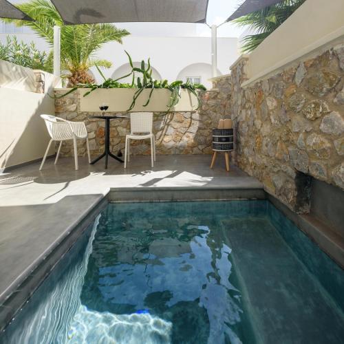 a pool with a table and chairs next to a stone wall at Afroditi Venus Beach Resort in Kamari