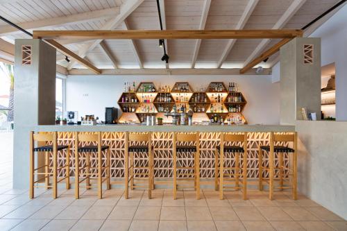 a bar with wooden stools and wine bottles at Hotel Hara Ilios Village in Gouves