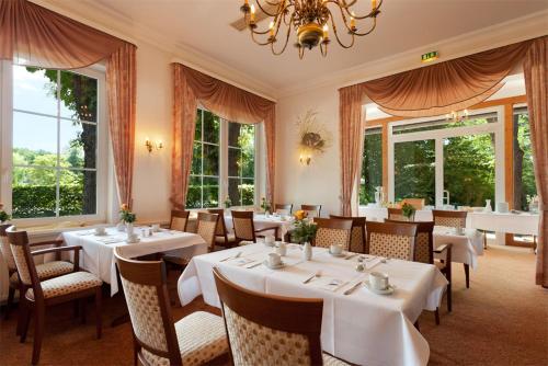 a restaurant with white tables and chairs and windows at Morada Hotel Isetal in Gifhorn