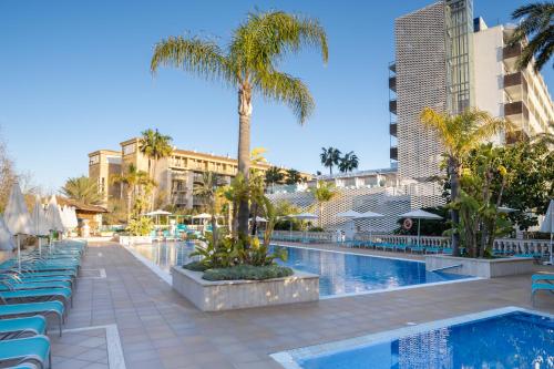una piscina con palmeras y edificios en Bahía de Alcudia Hotel & Spa, en Puerto de Alcudia