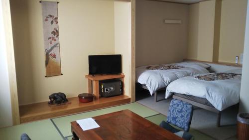 een kamer met twee bedden en een televisie en een tafel bij Oyado Nozawaya in Nozawa Onsen