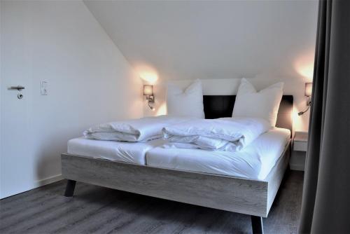uma cama com lençóis brancos e almofadas num quarto em Haus Nr 16, Ferienhaus Deichgraf em Wangerland