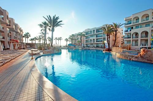 a swimming pool in a resort with palm trees and buildings at Grupotel Alcudia Pins in Playa de Muro