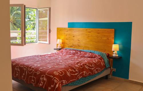 a bedroom with a bed with a wooden headboard and two windows at Villa Tilapia Tropical in Capesterre-Belle-Eau