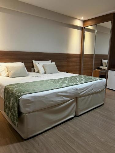 a bedroom with a large white bed with a green blanket at Vista Azul Apart Hotel - Vista Pinheiros in Pedra Azul