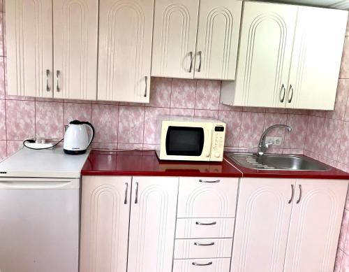 La cuisine est équipée de placards blancs, d'un four micro-ondes et d'un évier. dans l'établissement Квартира, à Tchernivtsi