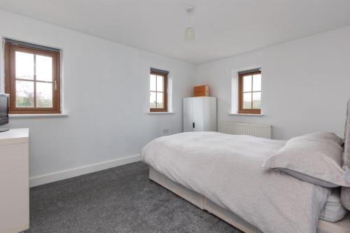 a white bedroom with a bed and two windows at Country cottage in Lower Bentham