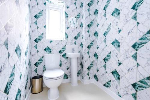 a bathroom with a toilet and green and white tiles at 4 Bed House Manchester By MCR Dens in Manchester