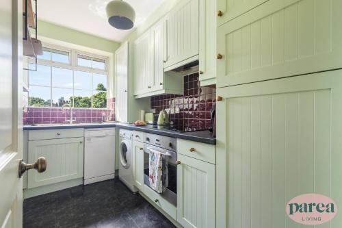 a kitchen with white cabinets and a washer and dryer at Parea Living - Stylish Islington 1-Bed Flat, 6min Walk to Tube in London