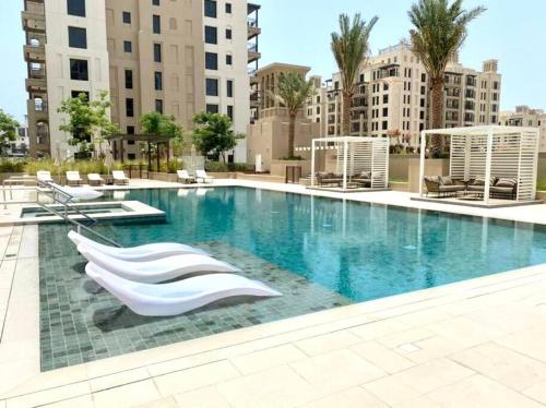 uma grande piscina com cadeiras brancas e edifícios em Dar Vacation - Bright and Charming 1 BR Apartment em Dubai