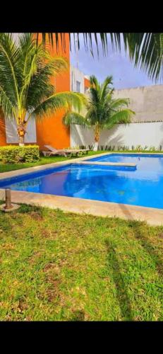 a swimming pool with palm trees next to a building at Depa con alberca en privada in Cancún