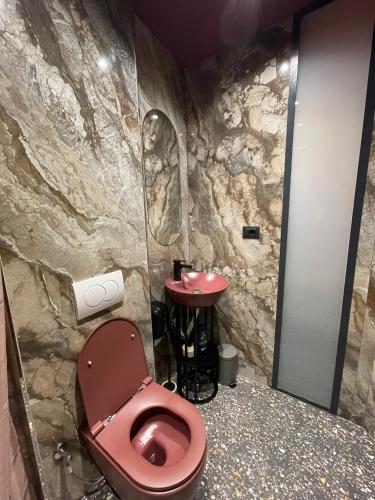 a bathroom with a red toilet and a stone wall at New Soho Hotel in Prizren