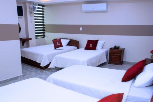 a room with three beds with white sheets and red pillows at Hotel MiKasa in Oliva