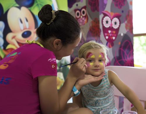 a young girl getting her face painted by a woman at Delphin Imperial Lara in Lara