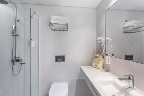 La salle de bains blanche est pourvue d'un lavabo et d'une douche. dans l'établissement B&B HOTEL Olhão Algarve, à Olhão