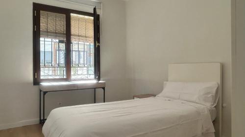 1 dormitorio con cama blanca y ventana en Casa en Los Remedios en Sevilla