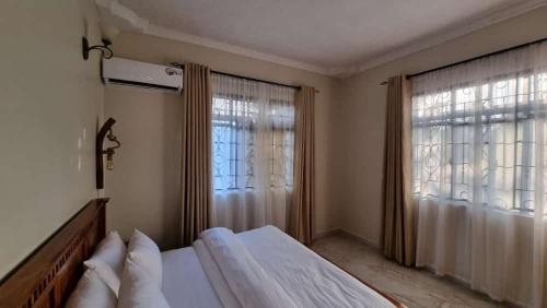 a bedroom with a bed and two large windows at Maisha Apartment in Msaranga