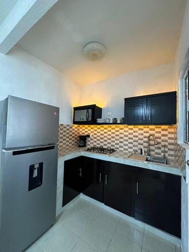 a kitchen with black cabinets and a stainless steel refrigerator at Depa con alberca en privada in Cancún