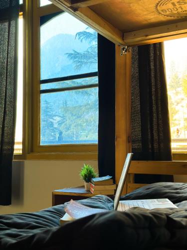 a laptop sitting on a bed in front of a window at Wabi Sabi Riverside Hostel in Kasol