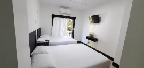 2 camas en una habitación blanca con ventana en HOTEL ARRECIFE, en Roatan