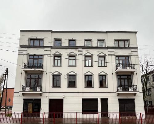 a white building with black windows and a fence at Brickller Apartments by Letrent in Żyrardów