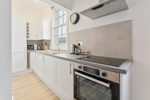 La cuisine est équipée de placards blancs et d'un four avec plaques de cuisson. dans l'établissement Modern 2 Bedroom Apartment in Central Cheltenham, à Cheltenham