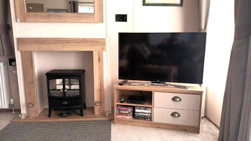 a entertainment center with a flat screen tv and a fireplace at Binka - Luxury 40 x 14ft Lodge in Tain