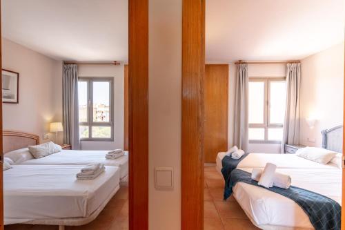 two beds in a room with two windows at Holiday beach homes Romaní II in Colònia de Sant Jordi