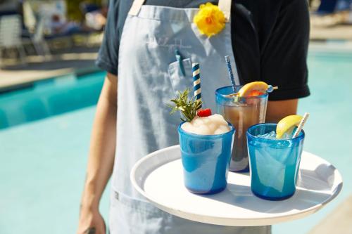 a person holding a tray with two cocktails on it at Holiday House Palm Springs in Palm Springs