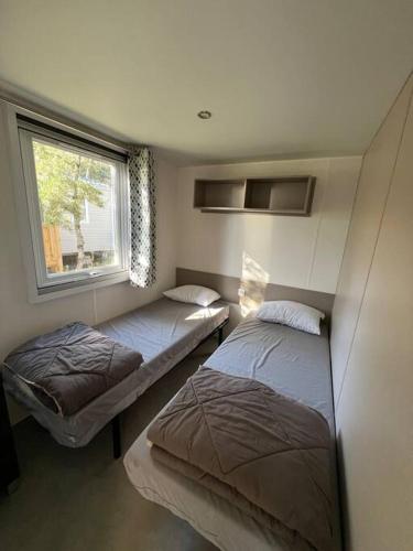 deux lits dans une petite pièce avec une fenêtre dans l'établissement mobilhome grand confort 6 couchages Cap Ferret, à Lège-Cap-Ferret