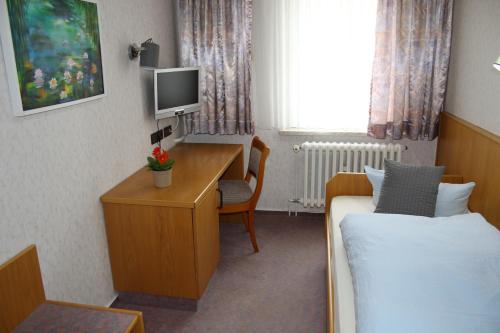 a hotel room with a bed and a desk with a television at Pension Erholung in Bad Elster