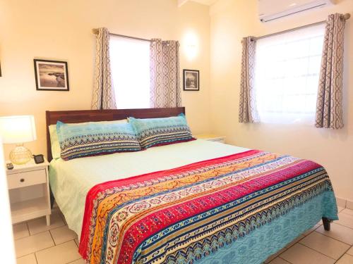 a bedroom with a bed with a colorful blanket and two windows at Ti Brico Gros Islet Bungalow in Gros Islet